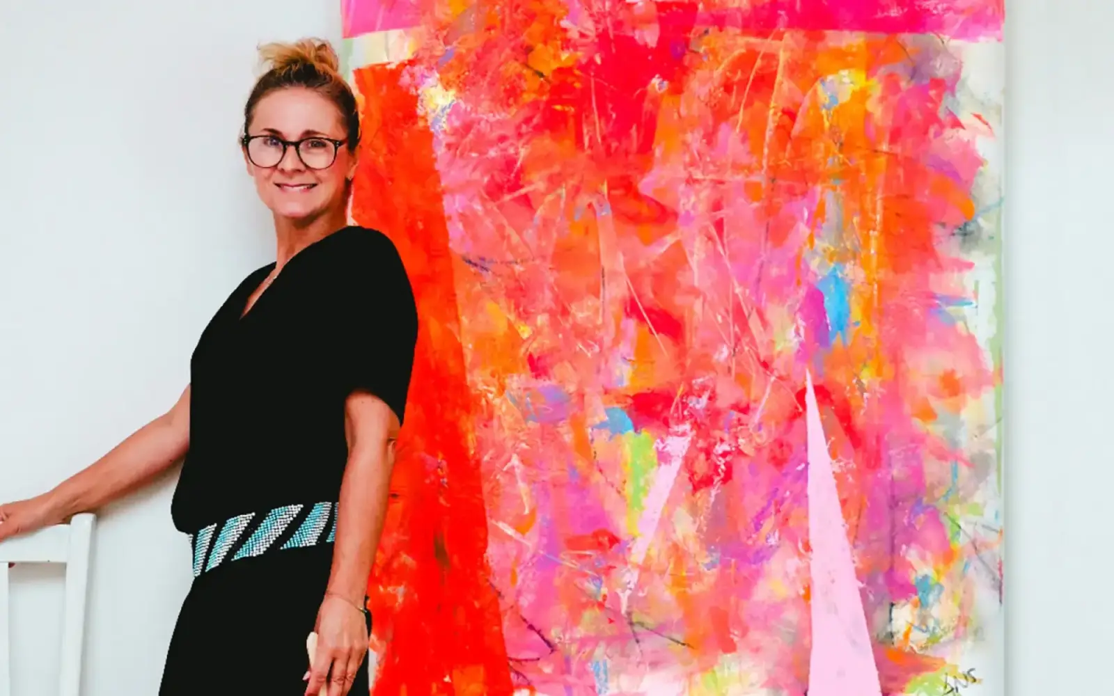 Die Künstlerin Annette Sandt steht vor einem ihrer lebendigen Werke, umgeben von knalligen Farben und pulsierender Energie.