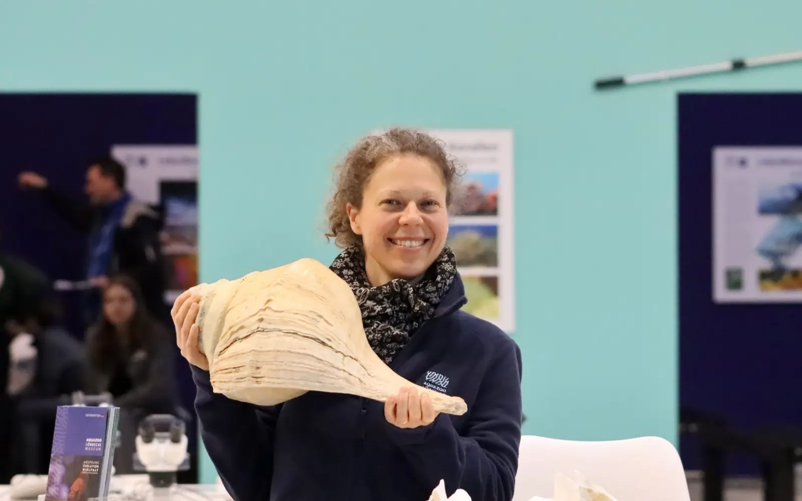 Eine Mitarbeiterin des Aquazoo Löbbecke Museums präsentiert ein beeindruckendes Schneckengehäuse am Messestand auf der boot 2026. Foto: Aquazoo Löbbecke Museum