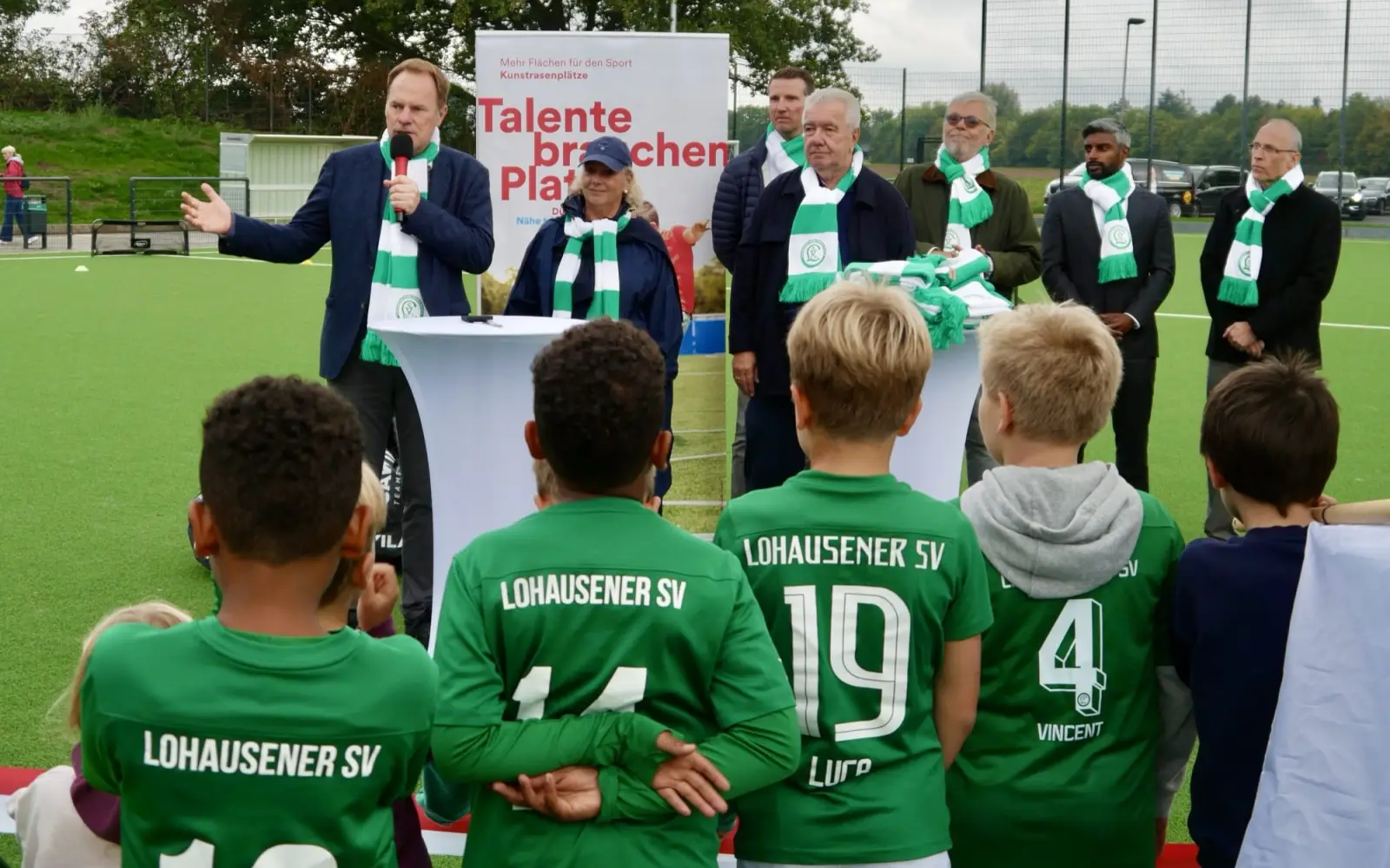 Oberbürgermeister Keller bei seiner Eröffnungsrede für den neuen Kunstrasenplatz in Lohausen. Im Bild mit ihm (von links): die stellvertretende Bezirksbürgermeisterin Babette de Fries, der Vorstand des Lohauser Sportvereins Peter Frymuth, Prinz Karneval Marcus Hülscher, Stadtsportbundpräsident Peter Schwabe, Flughafengeschäftsführer Pradeep Pinakatt und Förderer des Vereins. Foto: cj