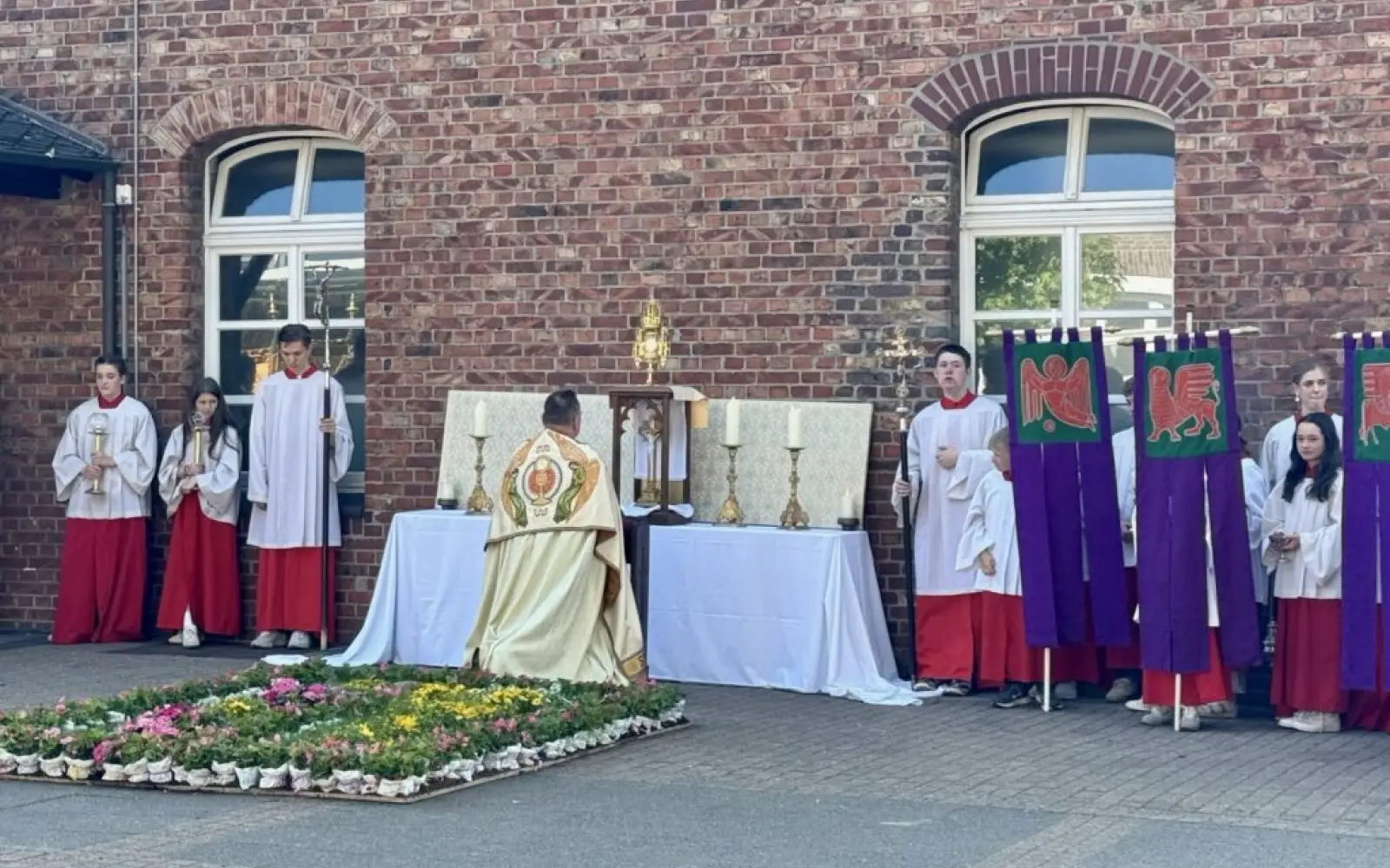 Ministranten und Gläubige versammeln sich zur Andacht am Außenaltar mit Blumenteppich auf dem Schulhof des Suitbertus-Gymnasiums. Foto: os