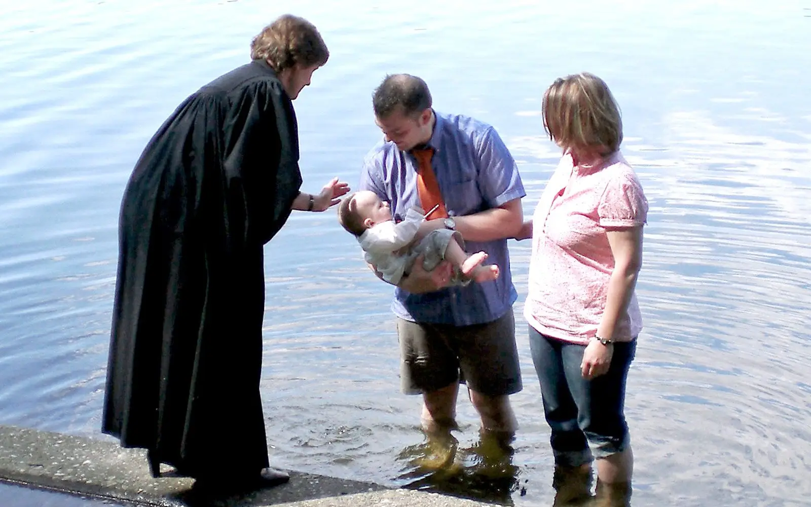 Archivfoto: Pfarrerin Ute Sawatzki tauft ein Kind im Wambachsee, begleitet von den Eltern, bei einem früheren Pfingstgottesdienst der Evangelischen Kirchengemeinde Trinitatis. Foto: trinitatis-duisburg.de