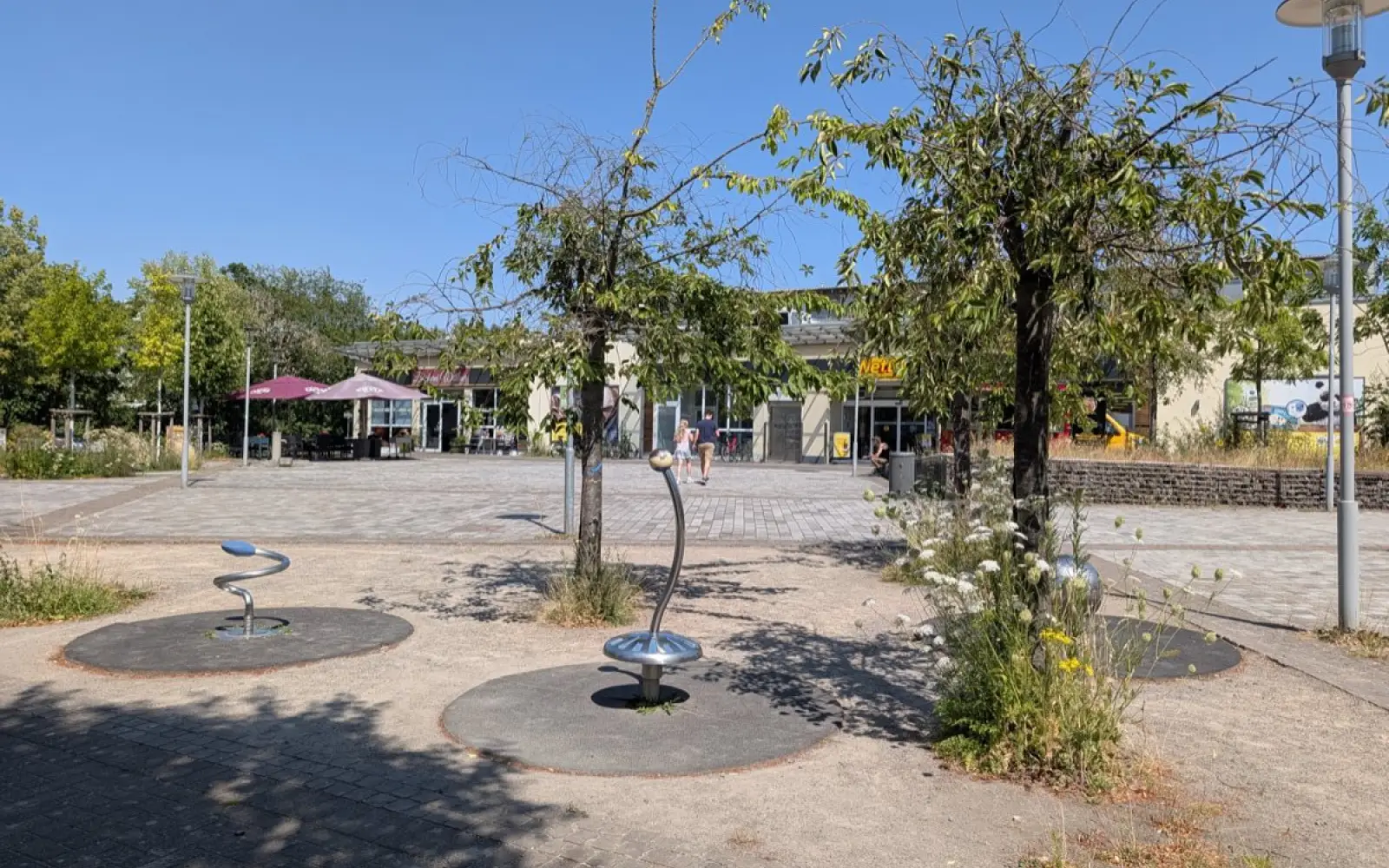 Vor der Bäckerei Wittlaer spenden Sonnenschirme den Schatten, den die vertrockneten Bäume auf dem Platz nicht mehr bieten. Foto: ah