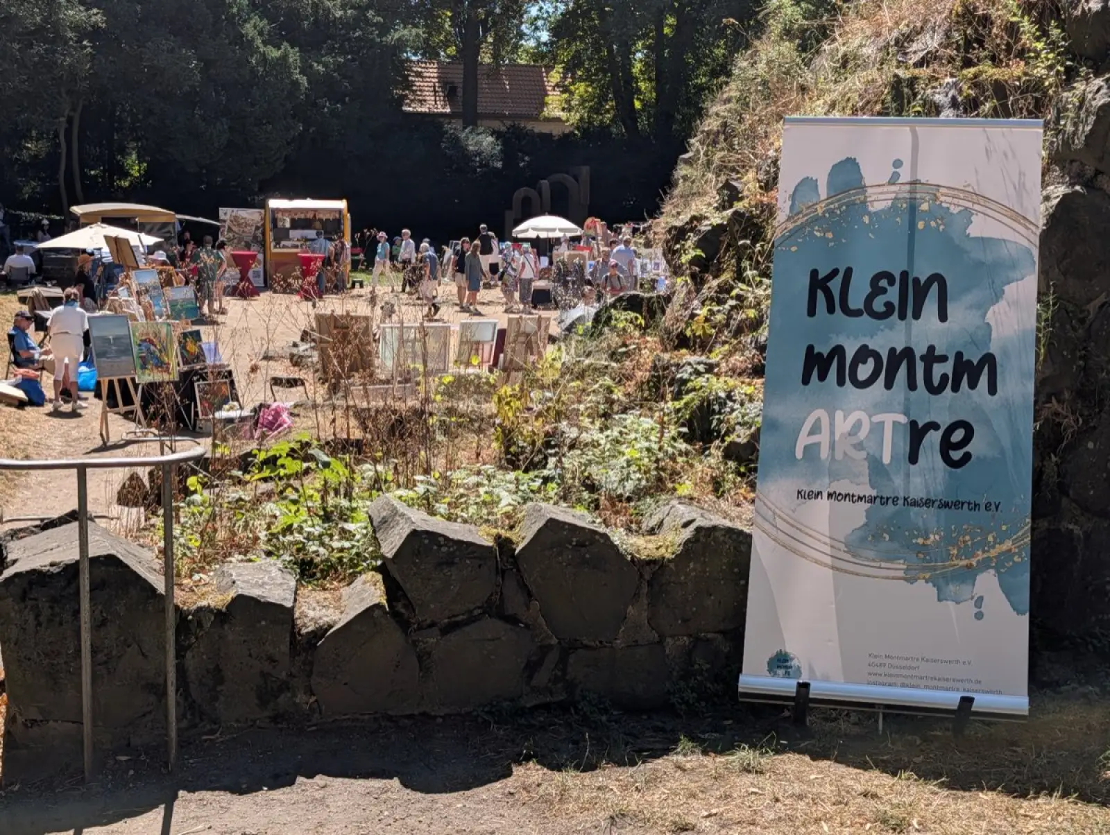Der Open-Air-Kunstmarkt Klein Montmartre hat sich am Fuß der Kaiserpfalz zwischen Burgmauer und Rheinufer aufgebaut.