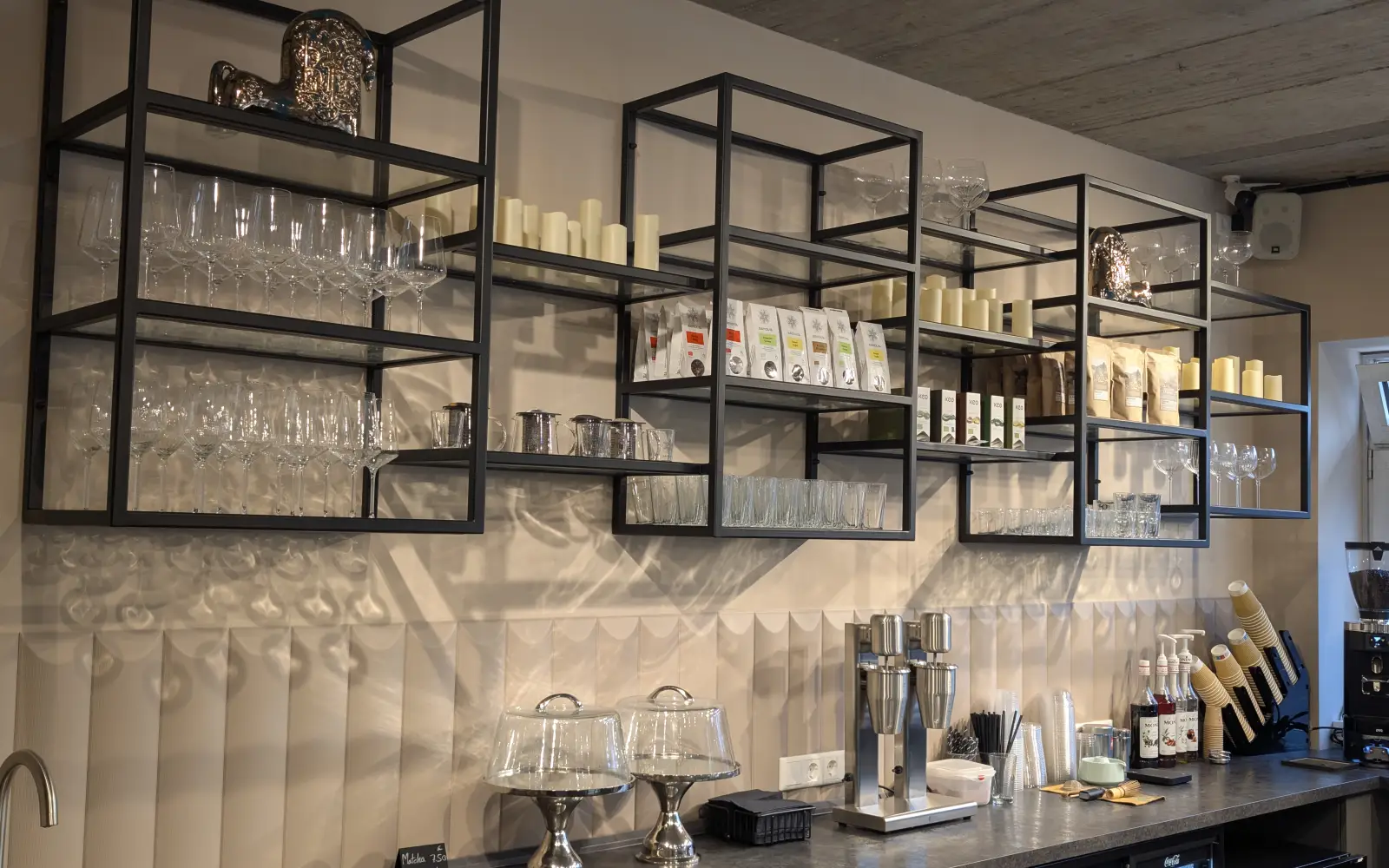 Hinter der Theke stehen Weingläser und Kaffeepackungen in schwarzen Stahlregalen. Foto: ah