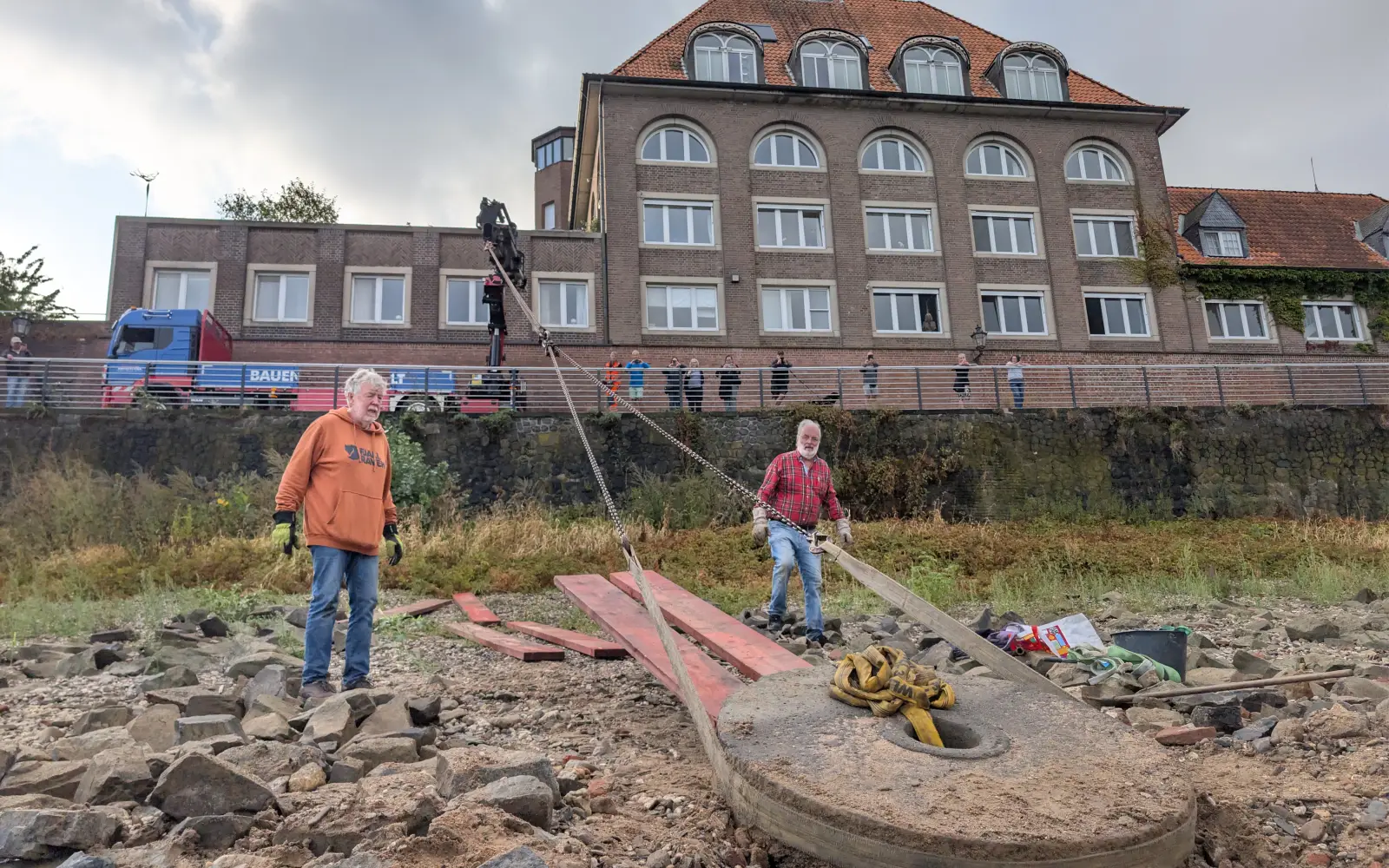 Über eine lange Kette holten die Helfer den Mühlenstein mit dem Kran die Uferböschung hinauf, oben verfolgten Zuschauer die Bergung. Foto: ah