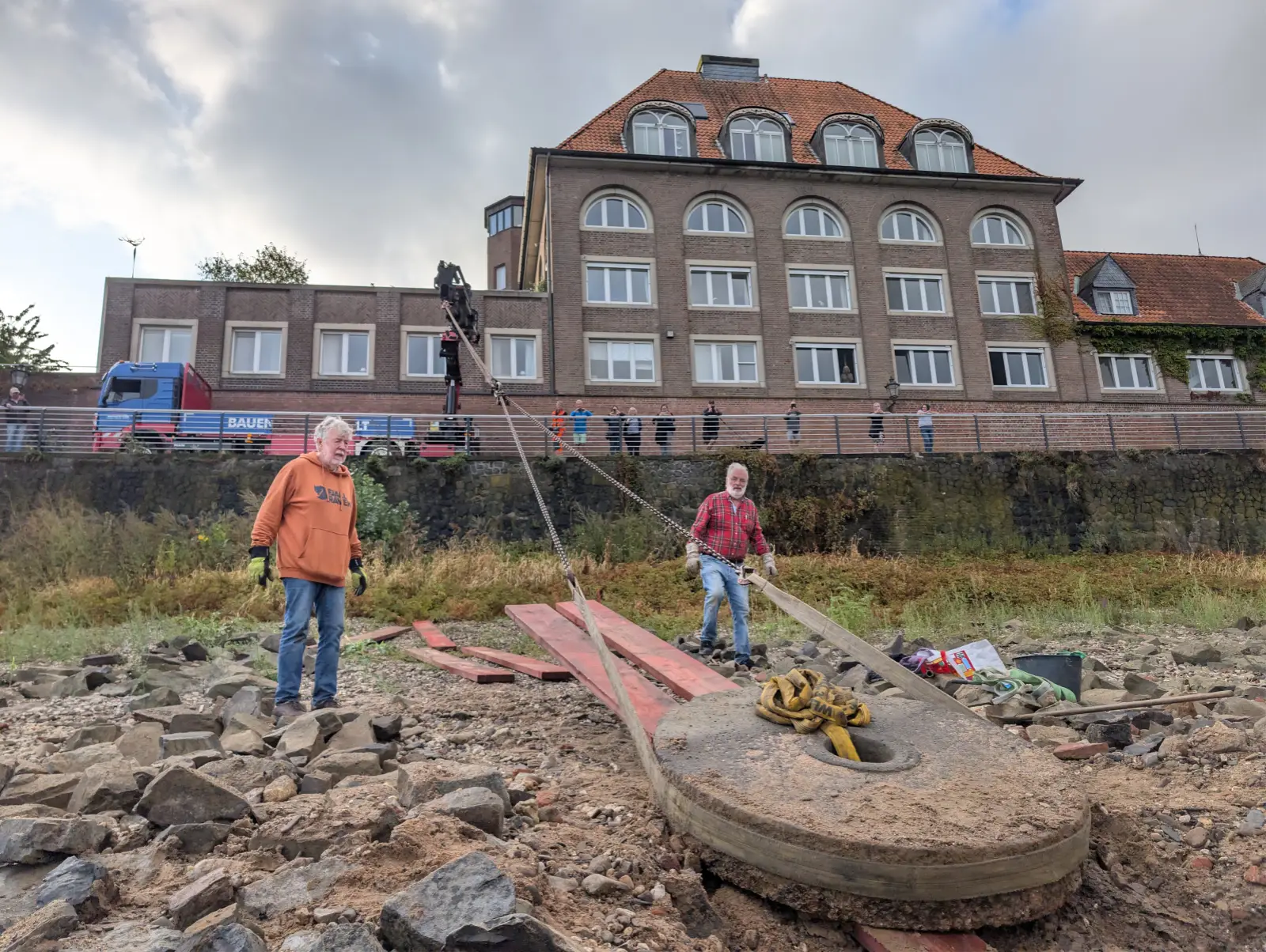 Über eine lange Kette holten die Helfer den Mühlenstein mit dem Kran die Uferböschung hinauf, oben verfolgten Zuschauer die Bergung. Foto: ah