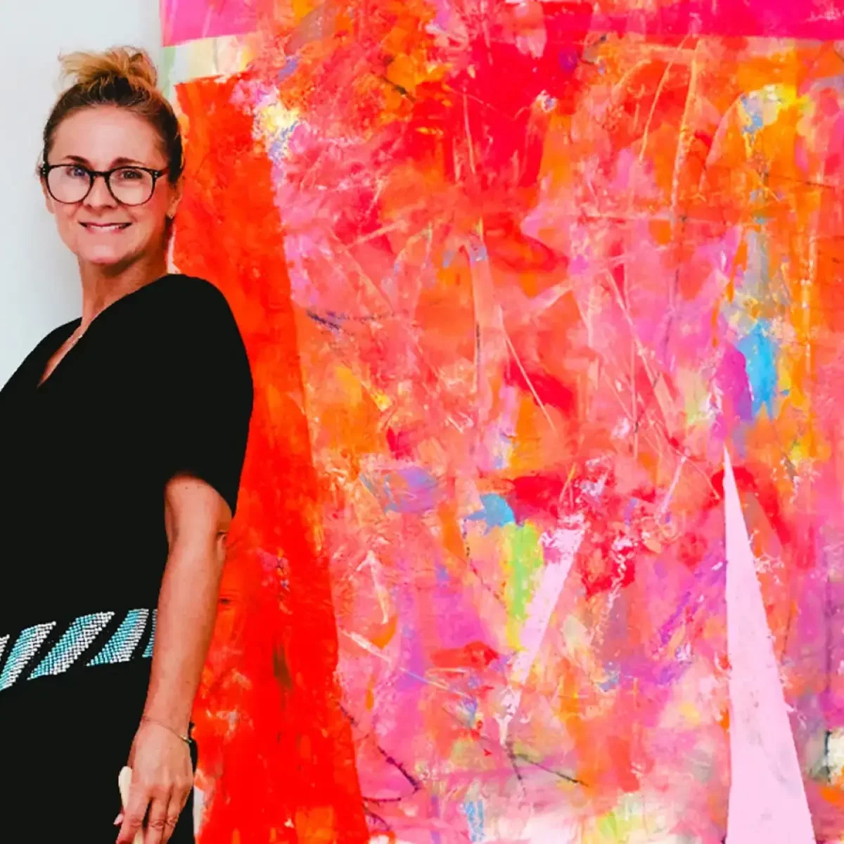 Die Künstlerin Annette Sandt steht vor einem ihrer lebendigen Werke, umgeben von knalligen Farben und pulsierender Energie.
