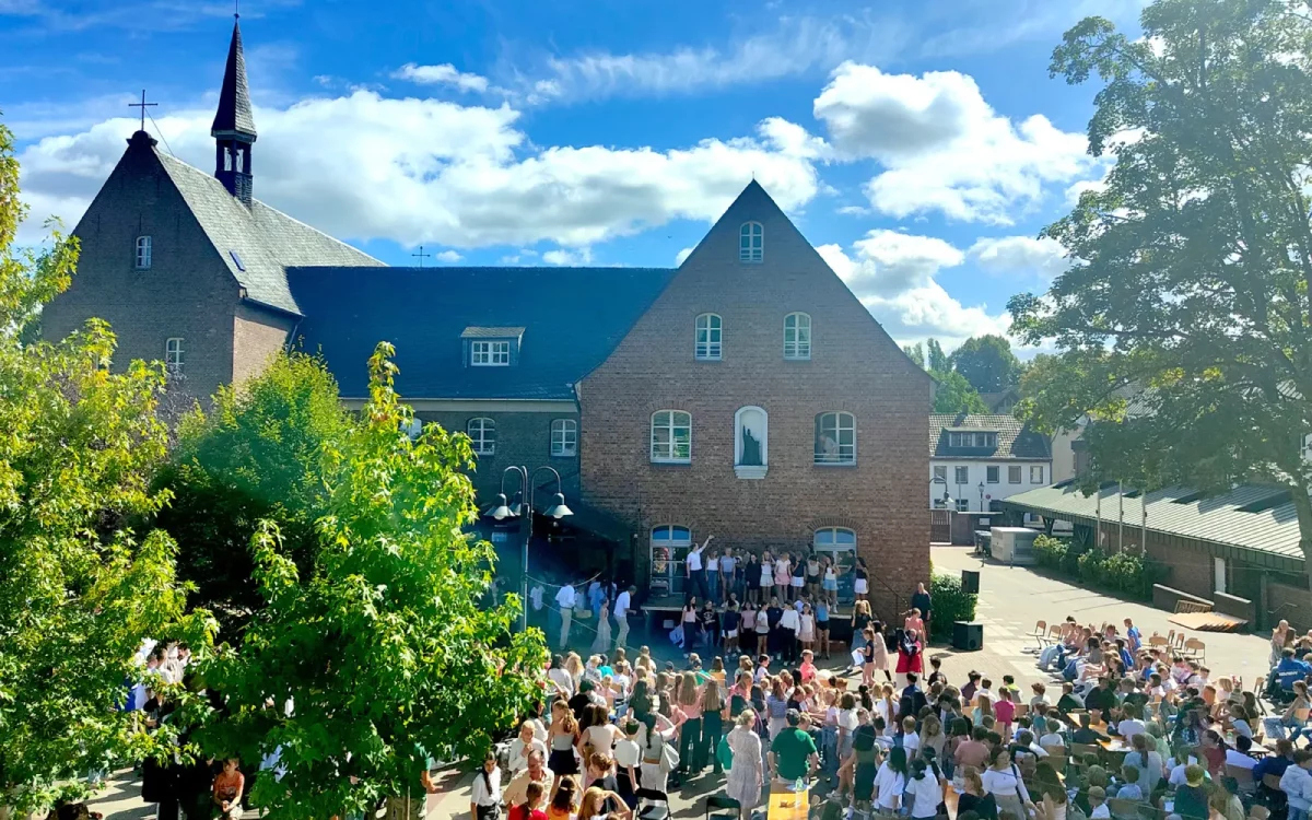 Schüle und Lehrer des Suitbertus-Gymnasiums feiern bei strahlendem Sonnenschein das Patroziniumsfest auf dem Schulhof, vereint unter dem Motto „Brücken bauen“. Foto: Antonia Kroll